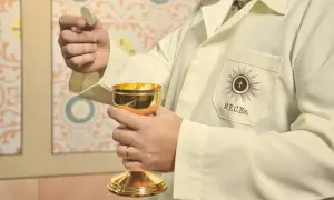 Dłoń trzymająca hostię i złoty kielich podczas ceremonii religijnej.