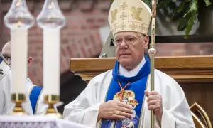 Kardynał w mitrze i szacie z pastorałem, trzyma rękę na piersi.