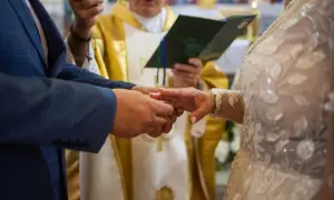 Para młoda wymienia obrączki podczas ceremonii ślubnej, z księdzem w tle.