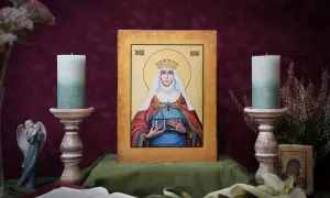 Ikona Świętej Łucji z koroną i budowlą w dłoniach, otoczona świecami i kwiatami.