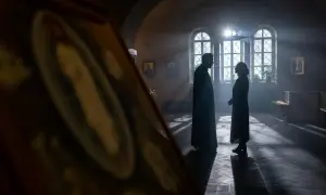 Sylwetki księdza i kobiety rozmawiających w kościele, w świetle wpadającym przez okna.