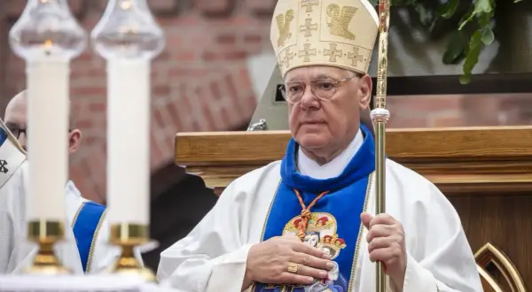 Kardynał w mitrze i szacie z pastorałem, trzyma rękę na piersi.