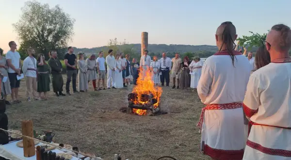 Grupa ludzi w strojach ludowych stoi wokół ogniska podczas obrzędu.