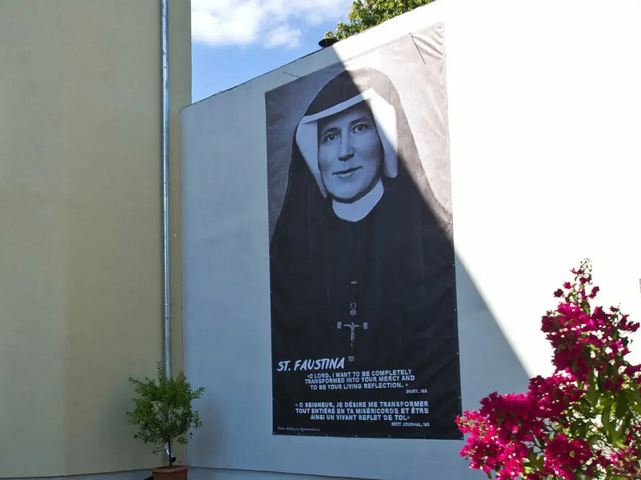 Plakat z portretem św. Faustyny na ścianie budynku, z napisem "ST. FAUSTINA".