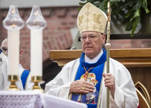 Kardynał w mitrze i szacie z pastorałem, trzyma rękę na piersi.